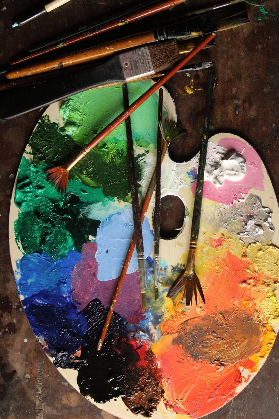 Wooden artist’s palette loaded with mixed colours and an assortment of paintbrushes