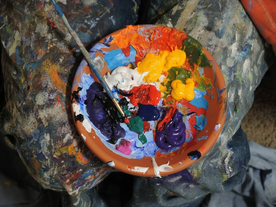 Paintbrush mixing bright acrylic colours on a round terracotta palette