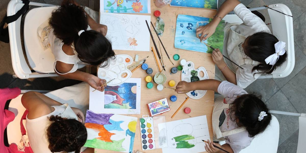 Overhead view of four children painting with watercolours around a shared art table