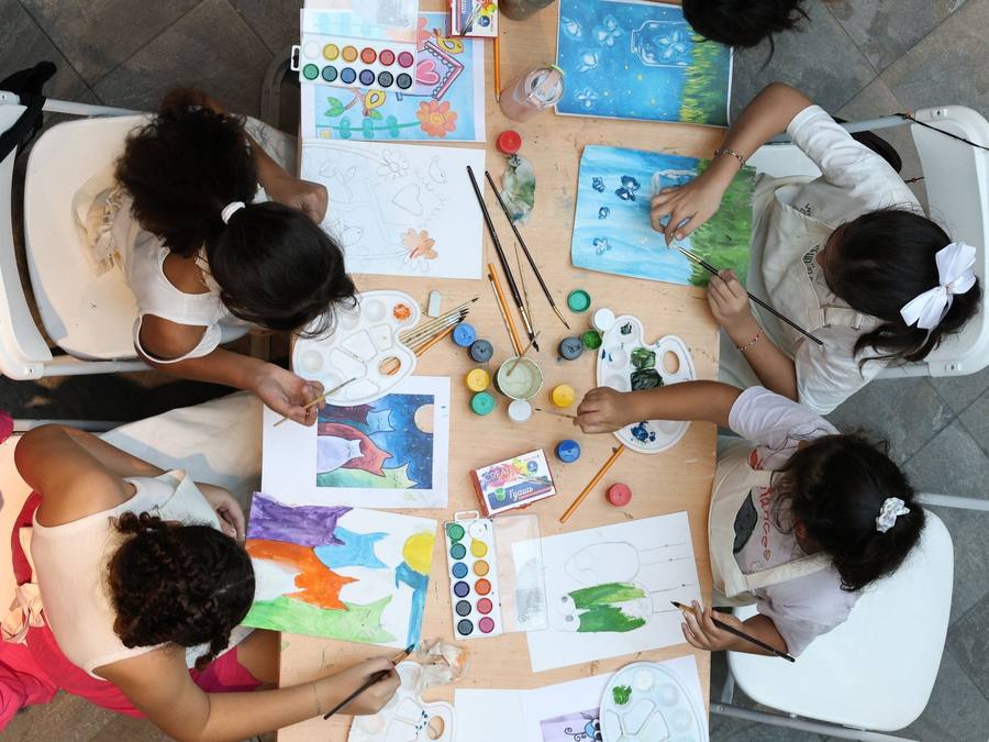 Overhead view of four children painting with watercolours around a shared art table