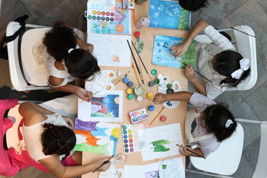 Overhead view of four children painting with watercolours around a shared art table