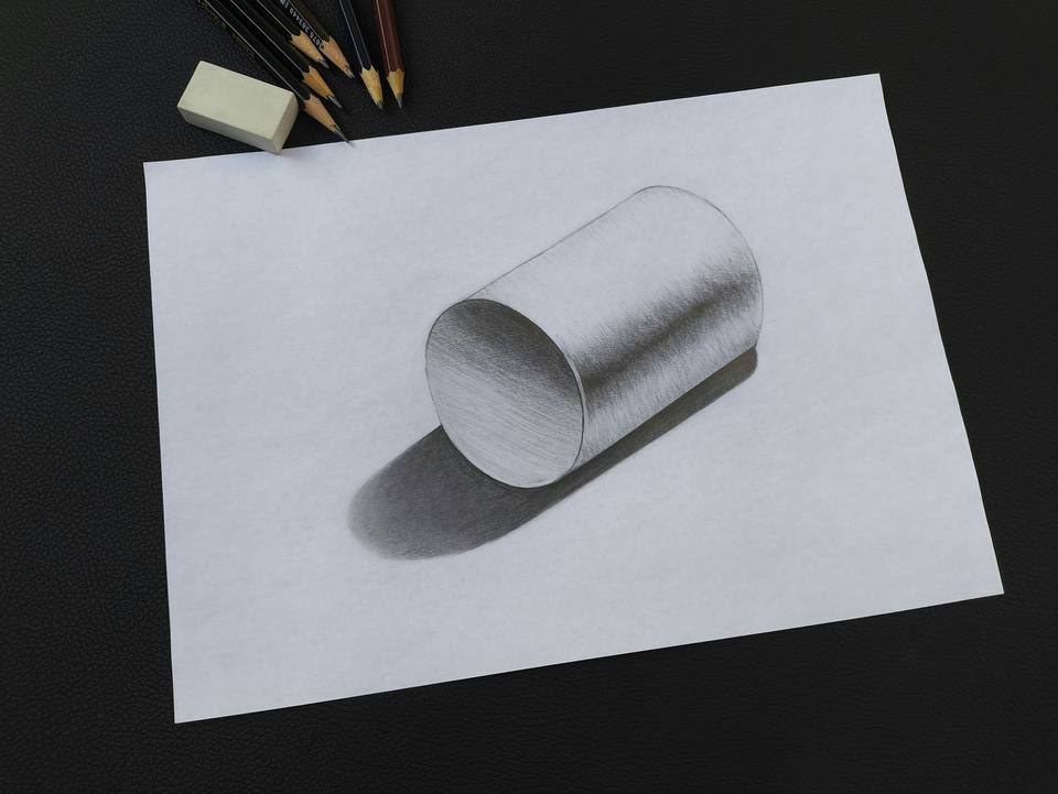 Graphite pencil drawing of a shaded cylinder with a cast shadow, pencils and eraser beside it