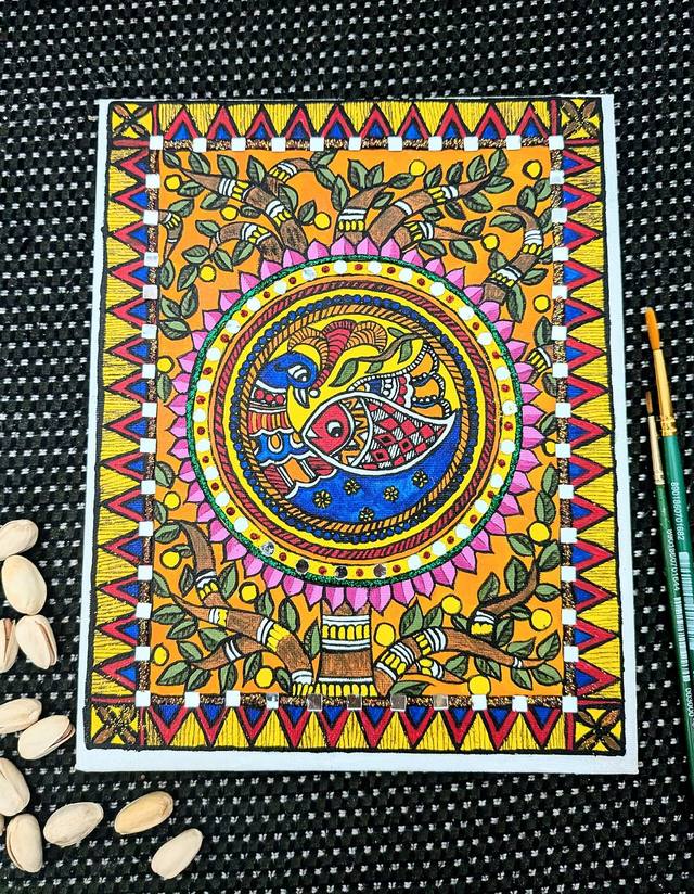 Madhubani painting of a peacock and fish in a circle, framed by leaves, lotus petals and triangle borders, with brushes beside it