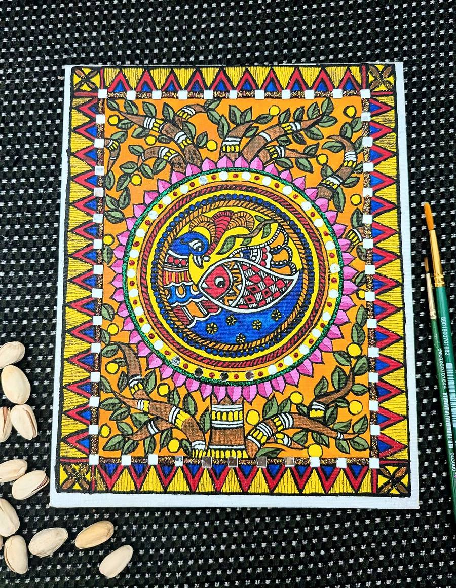 Madhubani painting of a peacock and fish in a circle, framed by leaves, lotus petals and triangle borders, with brushes beside it