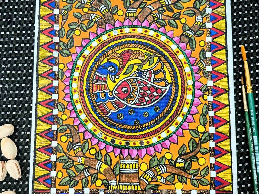 Madhubani painting of a peacock and fish in a circle, framed by leaves, lotus petals and triangle borders, with brushes beside it