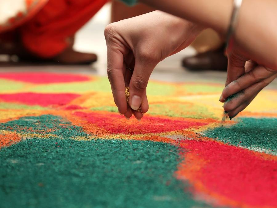 Hands sprinkling coloured powder to fill a red, green and yellow rangoli design
