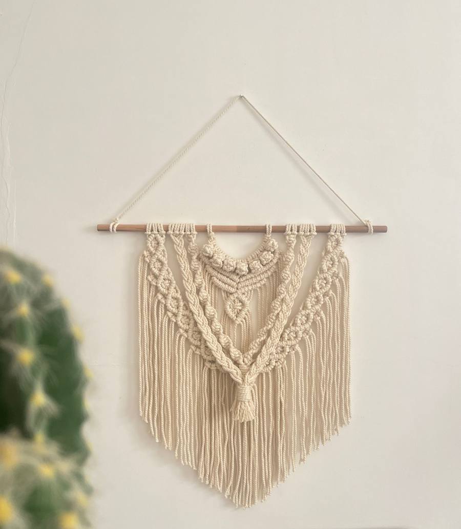 Handmade cream macrame wall hanging on a wooden dowel against a white wall