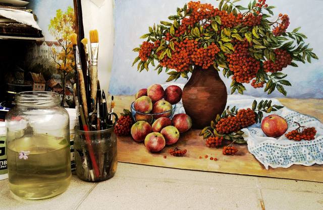Still-life painting of apples, berries and a clay vase beside a jar of paintbrushes