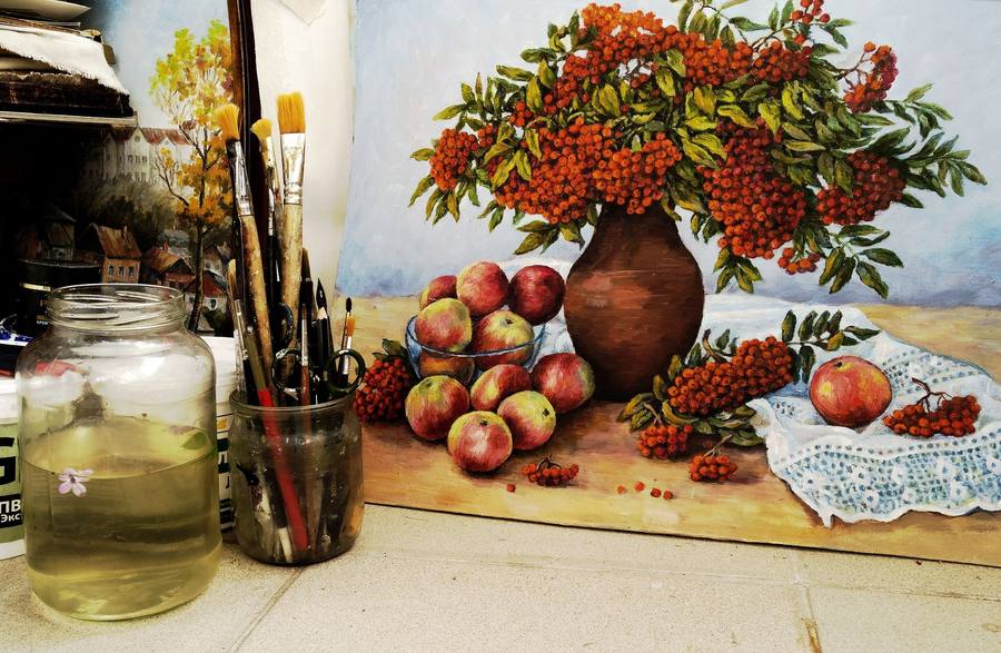Still-life painting of apples, berries and a clay vase beside a jar of paintbrushes