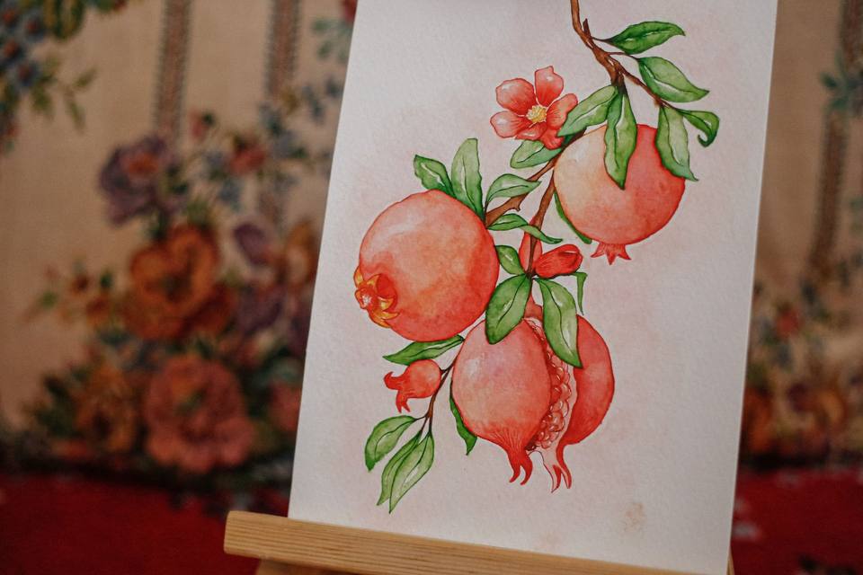 Watercolour botanical painting of pomegranates and leaves on a small easel