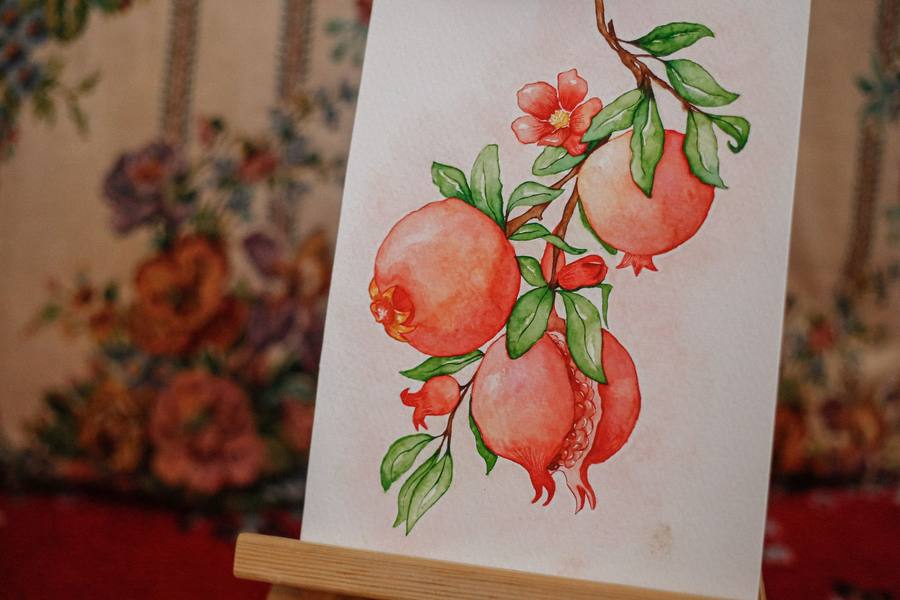 Watercolour botanical painting of pomegranates and leaves on a small easel