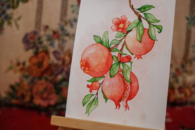 Watercolour botanical painting of pomegranates and leaves on a small easel