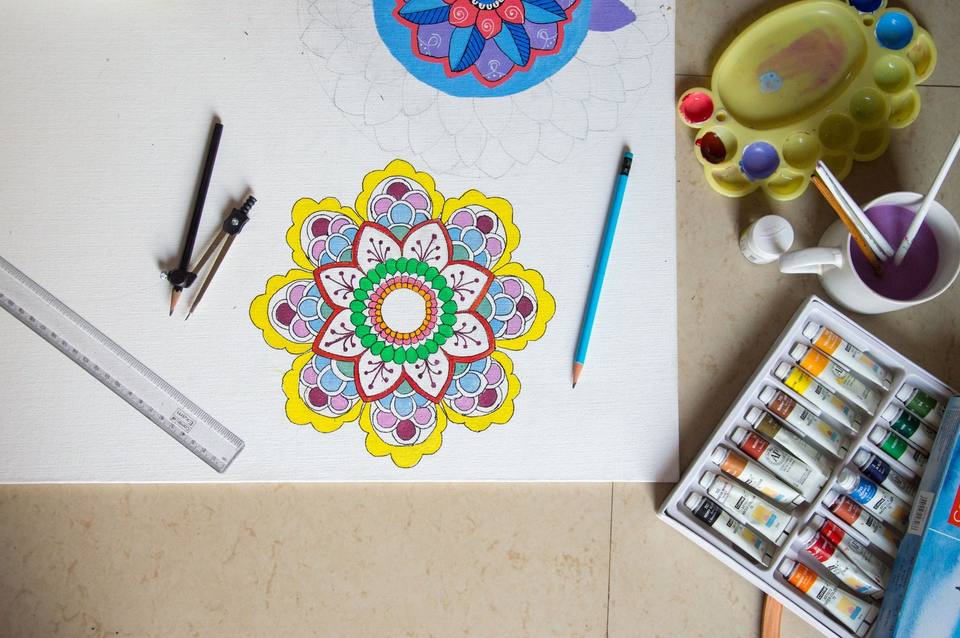 Colourful mandala drawing on white paper with pencils, ruler, compass and paints