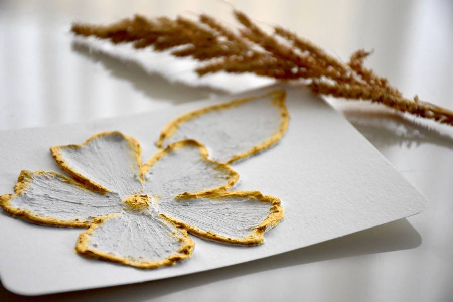 Handmade greeting card with a raised white-and-gold textured flower beside dried grass